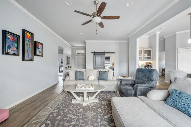 living area featuring wood finished floors, a ceiling fan, baseboards, ornamental molding, and a barn door