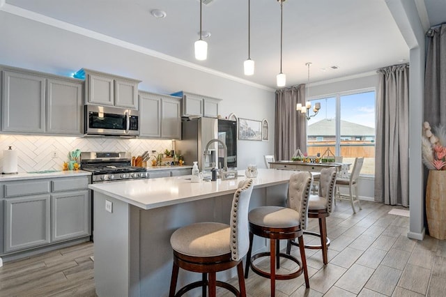 kitchen with backsplash, light countertops, ornamental molding, gray cabinets, and stainless steel appliances