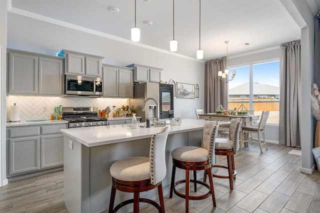 kitchen with decorative backsplash, ornamental molding, gray cabinets, and stainless steel appliances