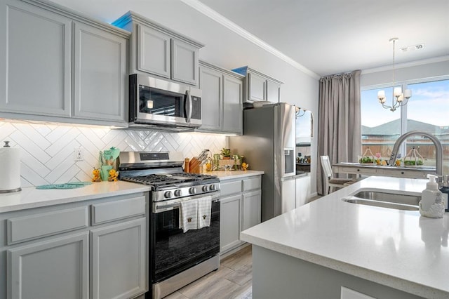 kitchen featuring backsplash, ornamental molding, gray cabinets, stainless steel appliances, and a sink