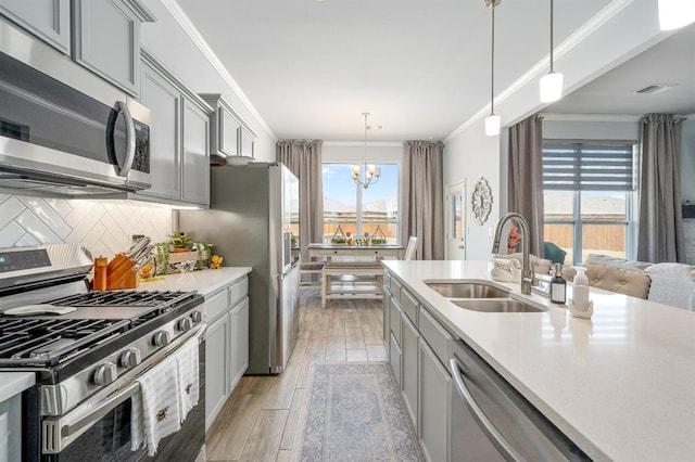 kitchen featuring gray cabinetry, ornamental molding, light wood-style floors, stainless steel appliances, and a sink