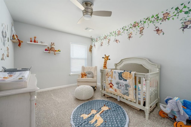 carpeted bedroom with a crib, baseboards, visible vents, and ceiling fan