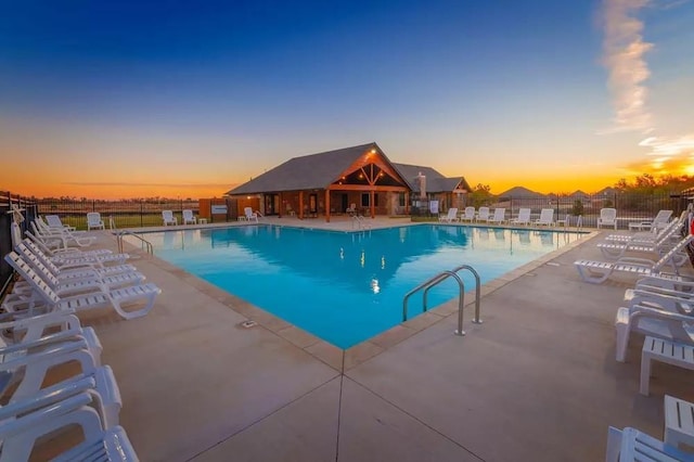 pool at dusk with fence, a community pool, and a patio area