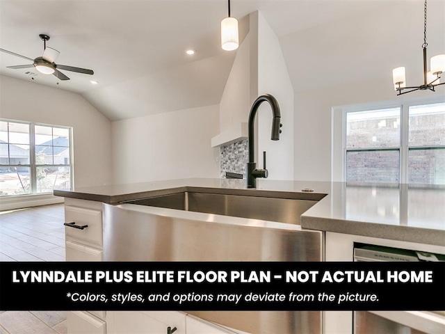 kitchen featuring a sink, vaulted ceiling, hanging light fixtures, white cabinets, and ceiling fan with notable chandelier