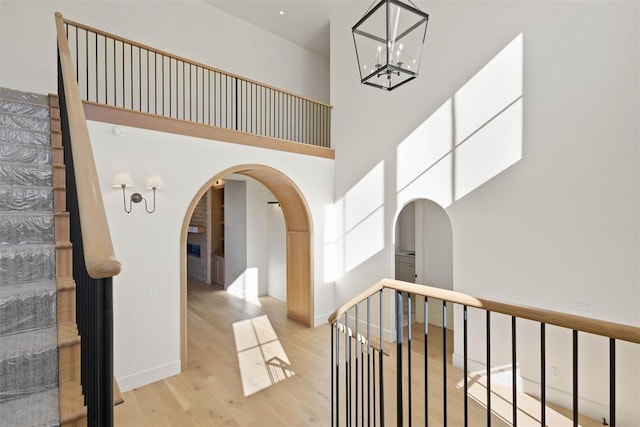 hall with baseboards, arched walkways, a towering ceiling, stairway, and wood finished floors