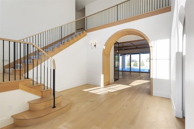 stairs with arched walkways, baseboards, a high ceiling, and wood finished floors