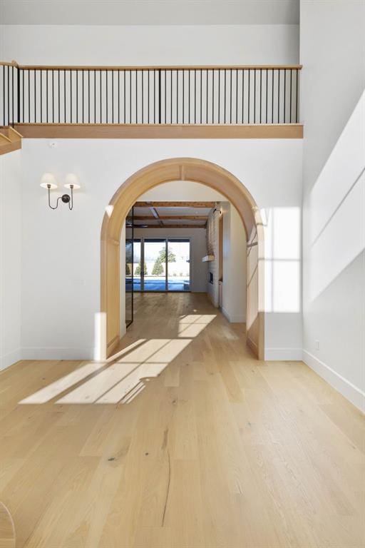 interior space featuring arched walkways, wood finished floors, a towering ceiling, and baseboards