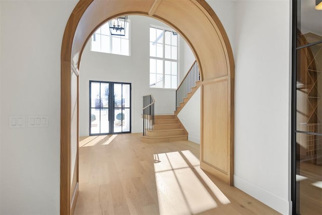 interior space with a healthy amount of sunlight, light wood finished floors, a towering ceiling, and stairway