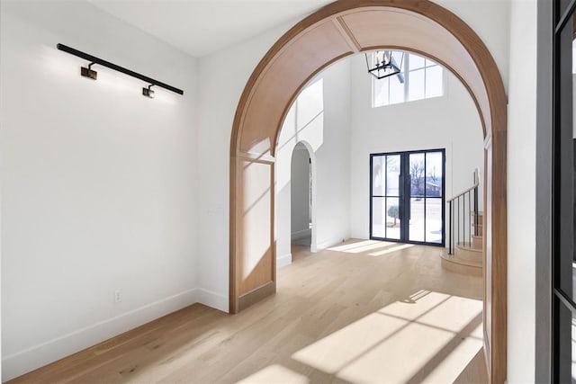 spare room featuring arched walkways, baseboards, light wood-style floors, french doors, and stairway