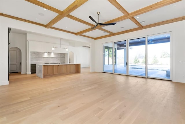 unfurnished living room with light wood finished floors, arched walkways, and coffered ceiling