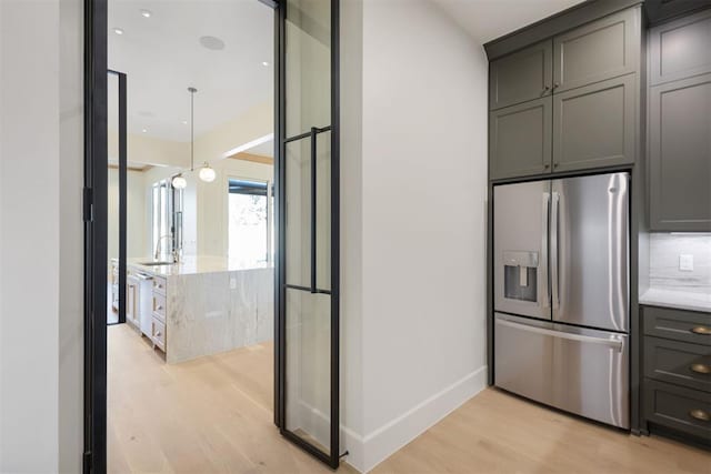 kitchen featuring baseboards, light wood-style flooring, light stone counters, stainless steel refrigerator with ice dispenser, and a sink