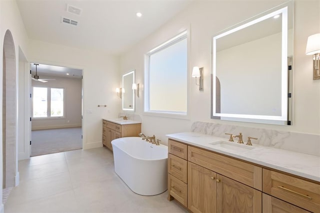 full bath with two vanities, a freestanding tub, visible vents, and a sink