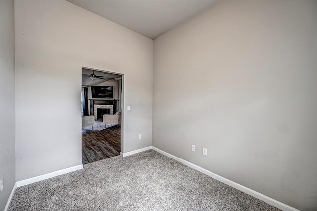 unfurnished room featuring carpet, baseboards, and a stone fireplace