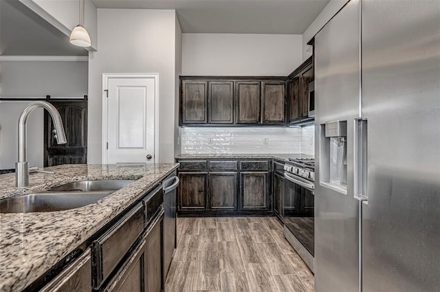 kitchen featuring light stone counters, stainless steel appliances, tasteful backsplash, a sink, and dark brown cabinets