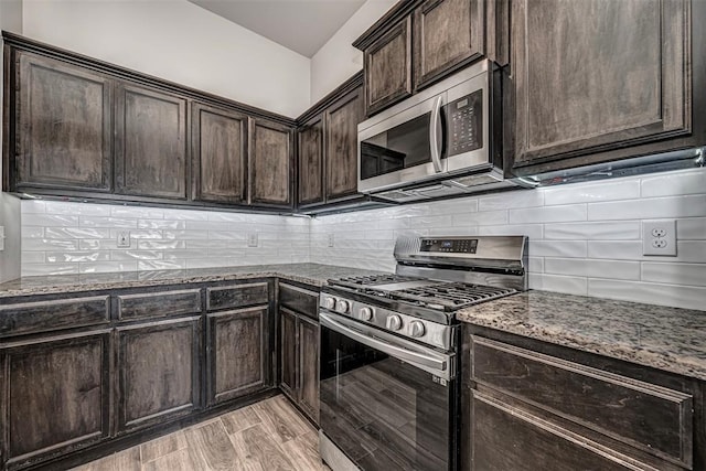 kitchen featuring light wood-style floors, dark brown cabinets, appliances with stainless steel finishes, dark stone counters, and tasteful backsplash