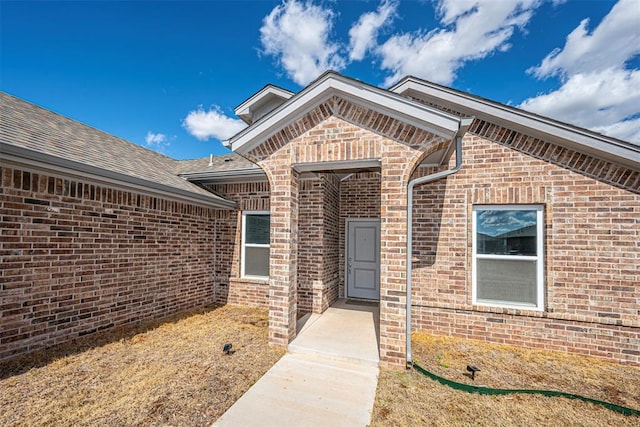 property entrance featuring a shingled roof and brick siding