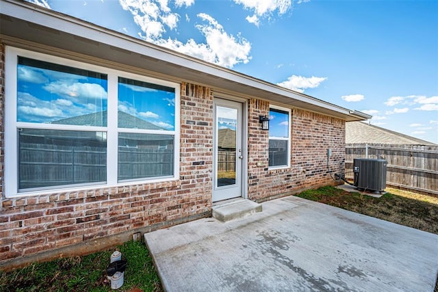 doorway to property featuring central AC unit, a patio area, fence, and brick siding