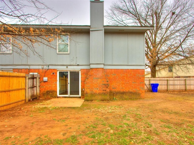 rear view of property featuring brick siding, fence, a chimney, and a patio