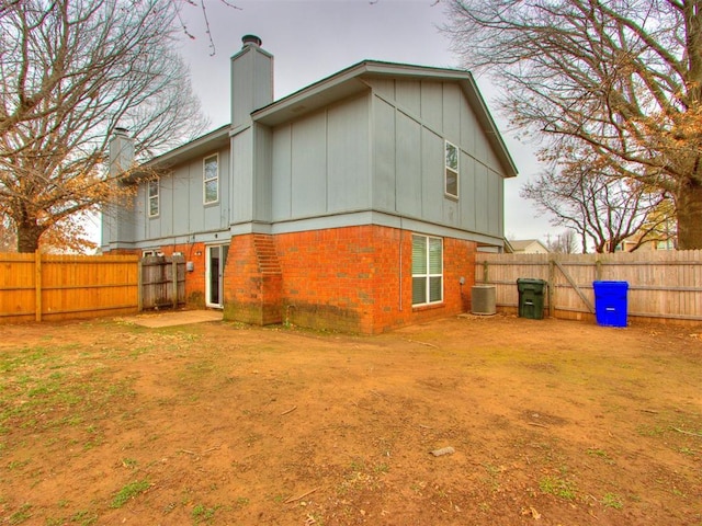 back of house featuring a fenced backyard, a chimney, central AC, and brick siding