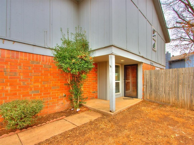 view of side of property featuring board and batten siding, brick siding, and fence