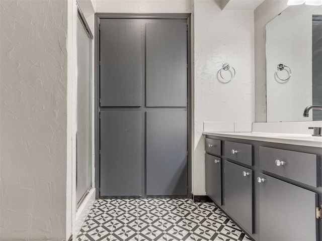 full bath with tile patterned floors, vanity, a shower with door, and a textured wall