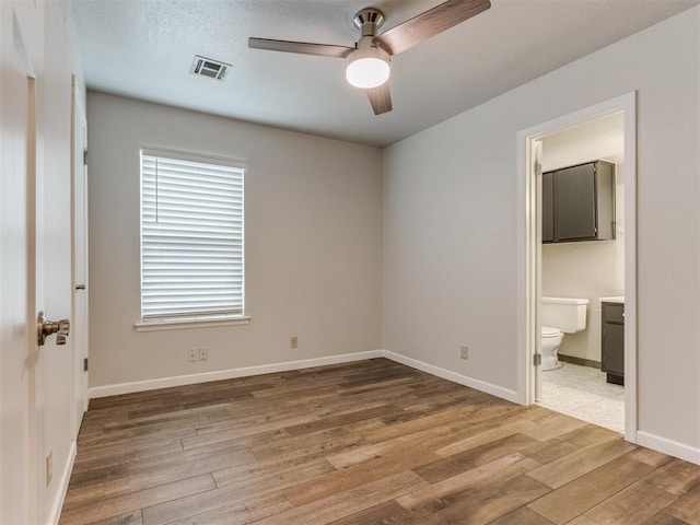 unfurnished bedroom featuring wood finished floors, a ceiling fan, visible vents, baseboards, and ensuite bath