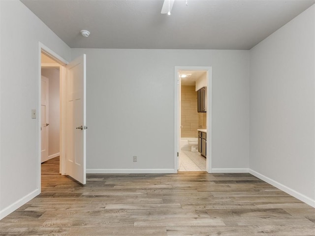 unfurnished bedroom featuring light wood finished floors, baseboards, a ceiling fan, and ensuite bathroom