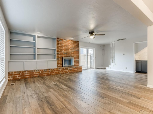 unfurnished living room with a brick fireplace, light wood-style flooring, visible vents, and a ceiling fan