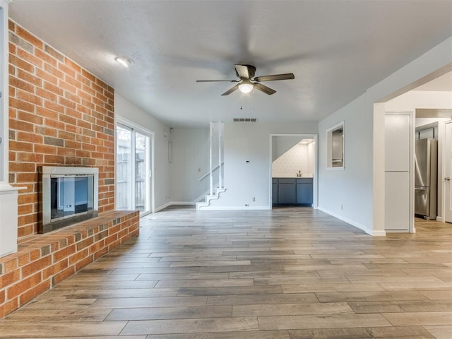 unfurnished living room with light wood-style floors, a brick fireplace, visible vents, and a ceiling fan