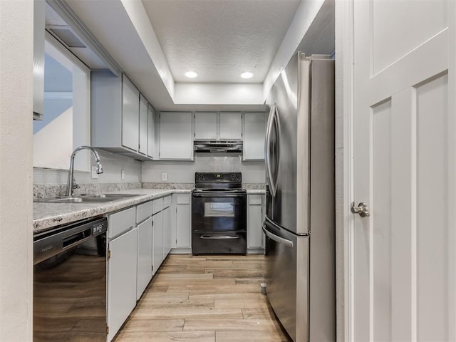 kitchen with light countertops, a sink, light wood-type flooring, under cabinet range hood, and black appliances