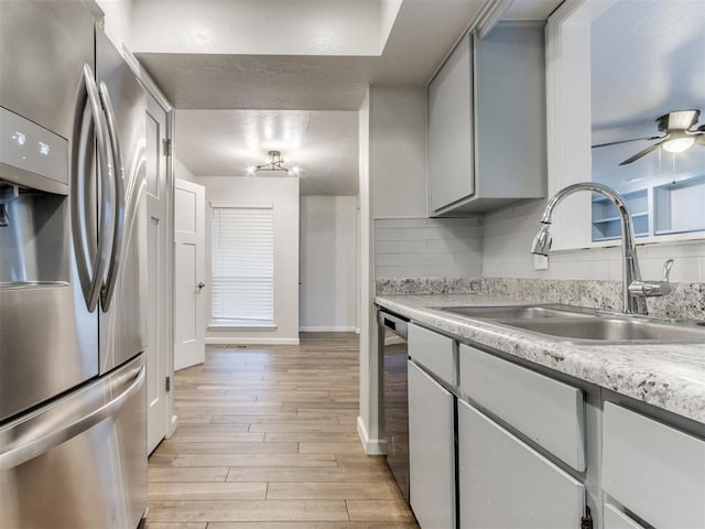 kitchen with stainless steel appliances, light countertops, backsplash, light wood-style flooring, and a sink