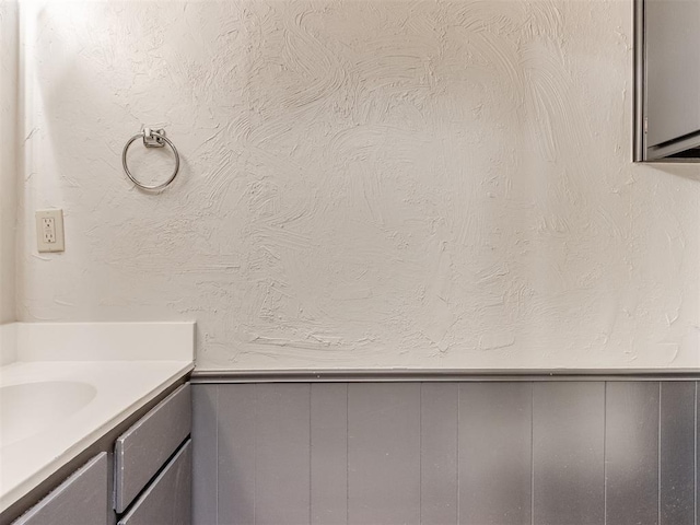 bathroom with a wainscoted wall, a textured wall, and vanity