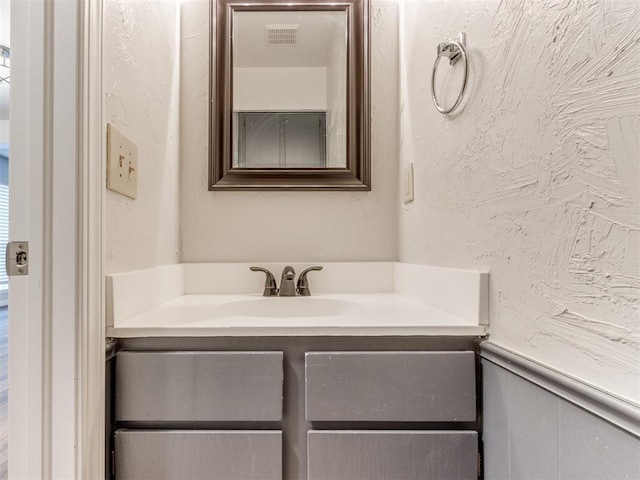 bathroom with vanity, visible vents, and a textured wall