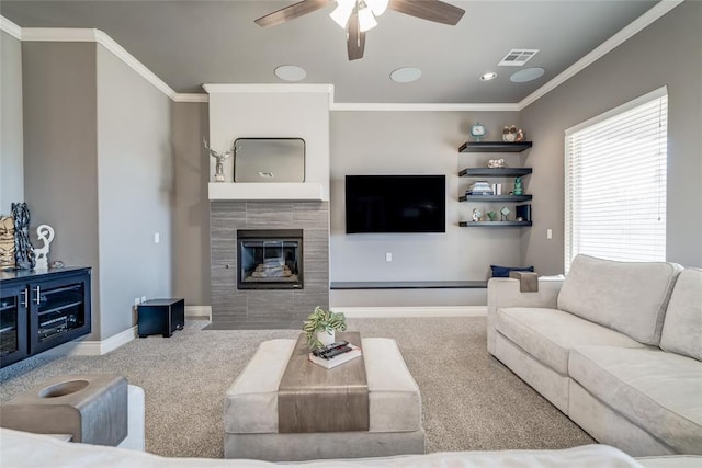 carpeted living room with visible vents, baseboards, ornamental molding, a tile fireplace, and a ceiling fan