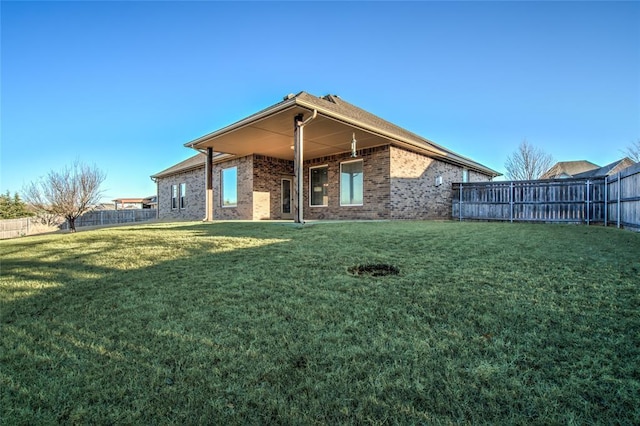 back of house with a lawn, brick siding, and a fenced backyard