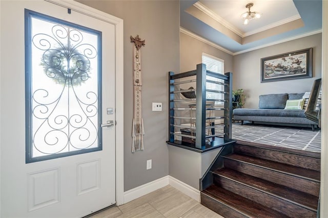 foyer featuring baseboards, a raised ceiling, and ornamental molding