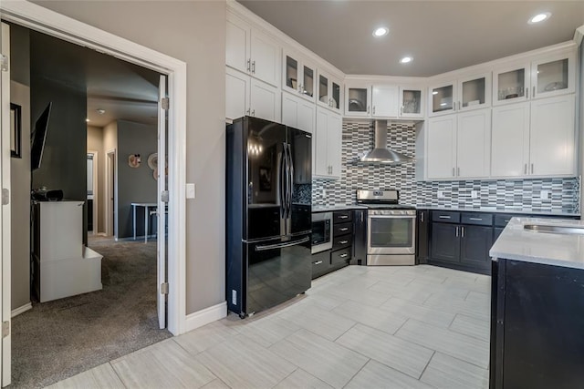 kitchen featuring wall chimney range hood, light countertops, decorative backsplash, appliances with stainless steel finishes, and white cabinets