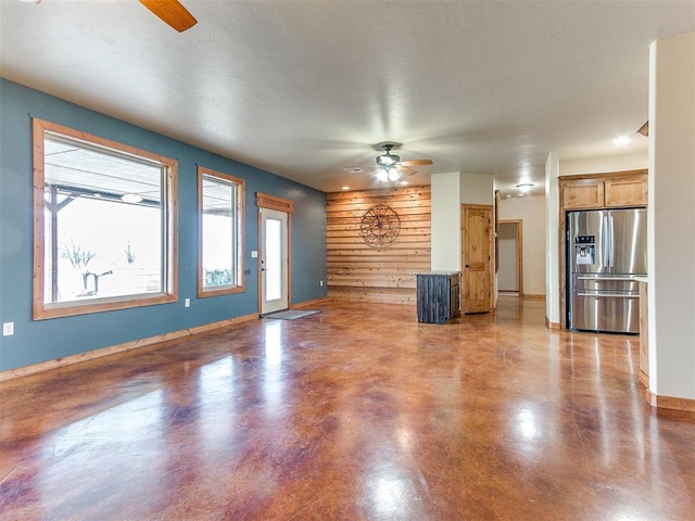 unfurnished living room with ceiling fan, baseboards, and concrete flooring