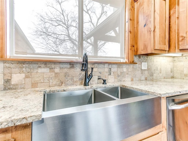 kitchen featuring stainless steel dishwasher, a sink, decorative backsplash, and light stone countertops