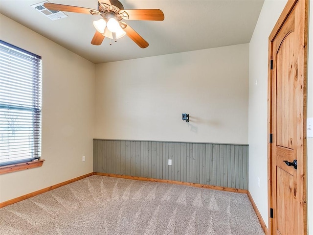 carpeted spare room featuring a wainscoted wall, ceiling fan, visible vents, and baseboards