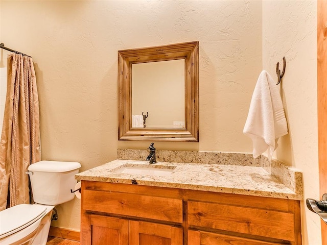 bathroom with a textured wall, vanity, and toilet