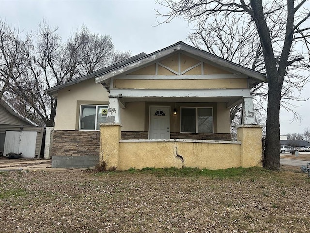 bungalow featuring stone siding, covered porch, and stucco siding