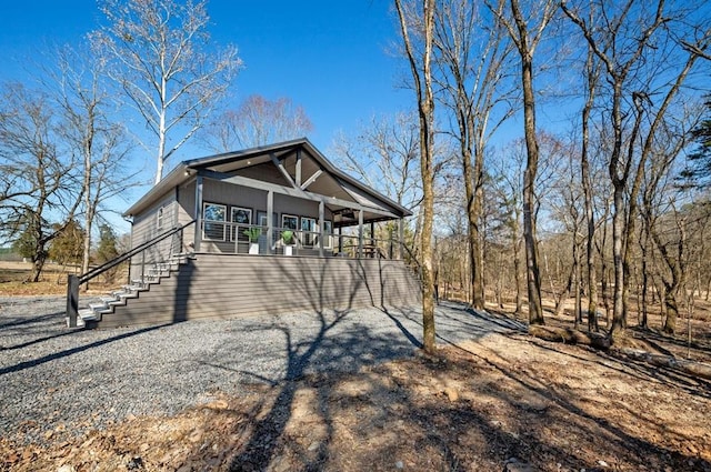 view of side of property with gravel driveway, covered porch, and stairs