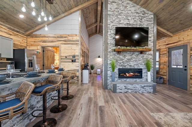 living area featuring a fireplace, wood ceiling, wooden walls, high vaulted ceiling, and light wood-type flooring