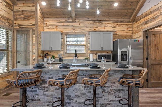 kitchen with stainless steel appliances, a kitchen breakfast bar, wood walls, and light wood finished floors