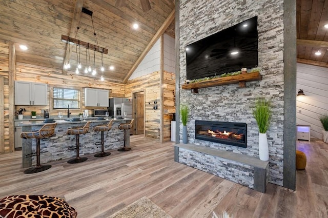 kitchen with high vaulted ceiling, wooden ceiling, a fireplace, light wood-style floors, and a kitchen bar