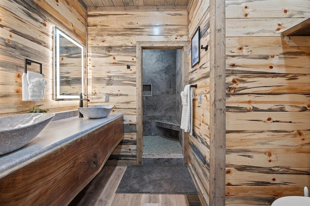 full bathroom with double vanity, a stall shower, wooden walls, and a sink