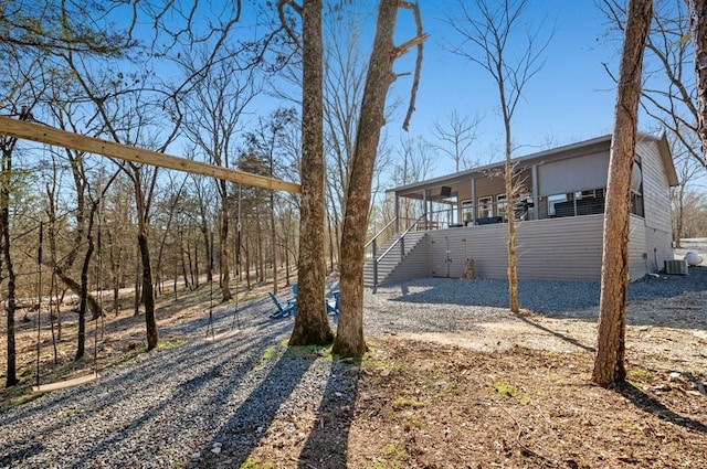 view of yard with stairs, a porch, driveway, and central AC unit