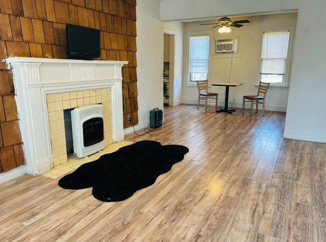 living area featuring baseboards, a tile fireplace, wood finished floors, heating unit, and an AC wall unit