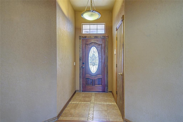 doorway with a textured wall, light tile patterned flooring, and baseboards